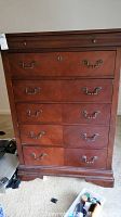 Front view of wooden chest showing five drawers with ornate metal handles and some scratches on the surface.