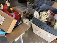 Plastic boxes filled with assorted Christmas decorations, garland, and other holiday items on a concrete floor.
