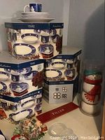 Stacked Sakura Snow Pals dinnerware boxes with one assembled place setting and snowman jar on counter