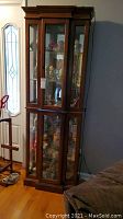 Full view of tall wooden curio cabinet with glass doors on upper and lower sections. Light cord visible on side.