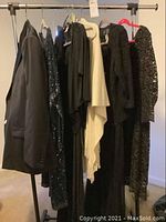 Metal clothes rack holding men's tuxedo and several women's long formal dresses along with an evening wrap or scarf.