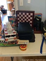 View of multiple stacked board games, wooden chessboard, black binoculars, toy fire truck, and Spot It game on table.