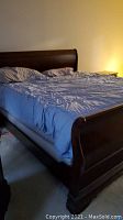 Assembled king sleigh bed showing dark wood headboard, footboard and side rails with bedding