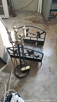 Photo showing fireplace log holder and set of four fireplace tools with brass handles on a stand.