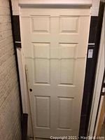 Front view of white 6-panel door in frame, standing vertically.