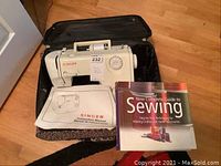 Singer sewing machine model E99670 in a leopard print soft carrying case with instruction manual and sewing guide book displayed alongside.