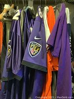 Photo showing multiple jerseys hanging including purple Baltimore Ravens jerseys with patches and numbers.