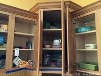 Kitchen cabinet showing Pyrex turquoise casserole dish, CorningWare dish with floral pattern, measuring cups, and a Crate and Barrel gravy boat.