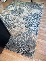 Full view of rectangular area rug on hardwood floor with visible swirling and knot-like abstract patterns in blue, grey and beige.