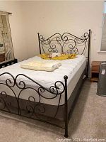 View of the full bed frame set up with a mattress and bedding, showing the headboard with decorative scrollwork.