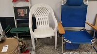 White plastic armchair and blue folding beach chair with wooden armrests and headrest, showing weathering.