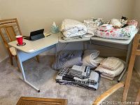 Corner computer desk in room with chair, white laminated top, white metal legs. Scratches noted on surface. Various linens and a cat on top and below desk not included.