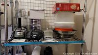 Shelf view showing various kitchen items including a food processor, metal bowls, containers, and accessories.