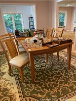 Full view of wooden dining table with multiple chairs arranged around it on patterned carpet, showing table surface and surrounding items.