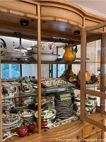 Wide image showing multiple shelves of china and serving dishes inside a wooden display cabinet, including plates, bowls, covered dishes, and decorative canisters shaped like fruit.