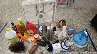 Lot items arranged on a garage floor including cleaning chemicals, bug spray, eyeglass cases, loofahs, pill cases, plastic bottles, and Sleep Phones headband.