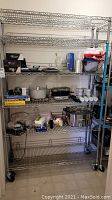 Full view of lot items on metal shelving including boxed appliances, cookware, ink cartridges, and dishware.