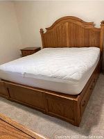 Full view of wooden platform bed with mattress in place and nightstand beside