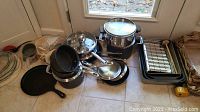 Photo showing assorted pots, pans, cast iron griddle, lids, and kitchen utensils arranged on the floor.