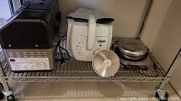 Photo of Presto deep fryer, Zojirushi bakery bread maker, and Universal Iron waffle maker on metal shelving.