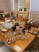 Overview showing multiple clear glass serving plates, bowls, cups, and small candle holders arranged on a table alongside wooden decorative items and spice rack.