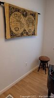 Photo of wall-hung globe tapestry above wood stool with floral needlepoint seat