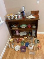Photo of a wooden shelf unit holding multiple Ireland mugs, glassware, plastic containers, and assorted vases and salt and pepper shakers arranged on and around it on floor