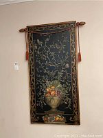 Rectangular wood art showing black background with fruit basket and vine details, bordered with gold scroll and hanging tassels.