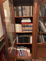 Books stored in a wooden cabinet on four shelves, with various colors and sizes, mostly Russian titles.