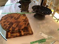 Overview photo showing all four items: two wood cutting boards stacked, large clear glass bowl, and black ceramic bowl on metal footed base.