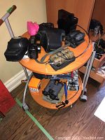 Overview photo of cameras and binoculars on a small oval table showing camera cases, binoculars, compact cameras.
