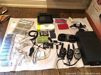 Overview of all items including cameras, GPS, walkie-talkies with chargers, string lights, and accessories arranged on white cloth