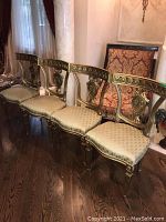 Front view of four gilded wood chairs arranged in a row on hardwood floor