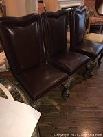 Front view of four chairs showing brown leather upholstery and carved gilt wood legs