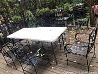 Wide shot showing folding table and six wrought iron chairs in outdoor patio setting with leaves scattered on surfaces.