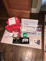 Wide shot of entire lot on floor including red iRestore boxes, Obagi kit, green Kerastase box, Caudalie card, hair ties, Epsom salt, small boxed items, nail polish