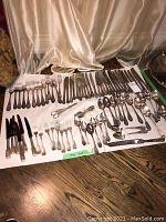 Full layout of silver plated cutlery on a white cloth including forks, knives, spoons, and serving pieces.