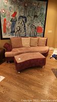 Front view of curved sofa and matching curved ottoman, with four beige pillows and metal legs visible
