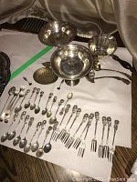 White background showing assorted sterling flatware and serving pieces, including spoons, forks, compotes, trivet