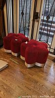 Two red floral-shaped stools positioned side by side on hardwood floor in front of glass doors