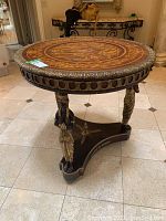 Front three-quarter view of round wooden high table showing marquetry top, carved gilt legs and triangular base