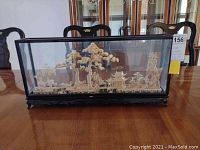 Front view of the glass encased diorama showing the entire scene including trees, architectural structures and landscape.