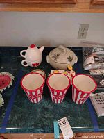 Overall view of seven pieces including teapot, casserole dish, popcorn buckets, and figurine.