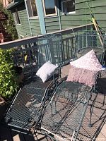 Photo showing two matching metal chaise lounges with cushions placed on an outdoor wooden deck railing visible.