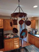 View of full copper pot rack hung in kitchen with seven copper items hanging including ladle, scoops, saucepans and pans.