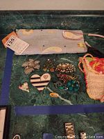 Seven costume jewelry pieces arranged on a green marble surface with two fabric bags, one blue paisley and one peach crocheted bag.