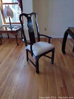 Full view of a two-armed wooden dining chair with upholstered seat and dark finish on hardwood floor.
