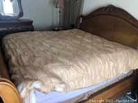 Photo showing California king-size gold comforter with visible wear and tears on a classic wooden bed frame