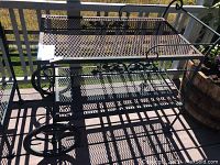 Top and side view of weathered metal serving cart on deck, showing mesh shelf and decorative metal scrollwork.