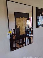 Full view of rectangular mirror with black frame and central embossed kimono design in gold.